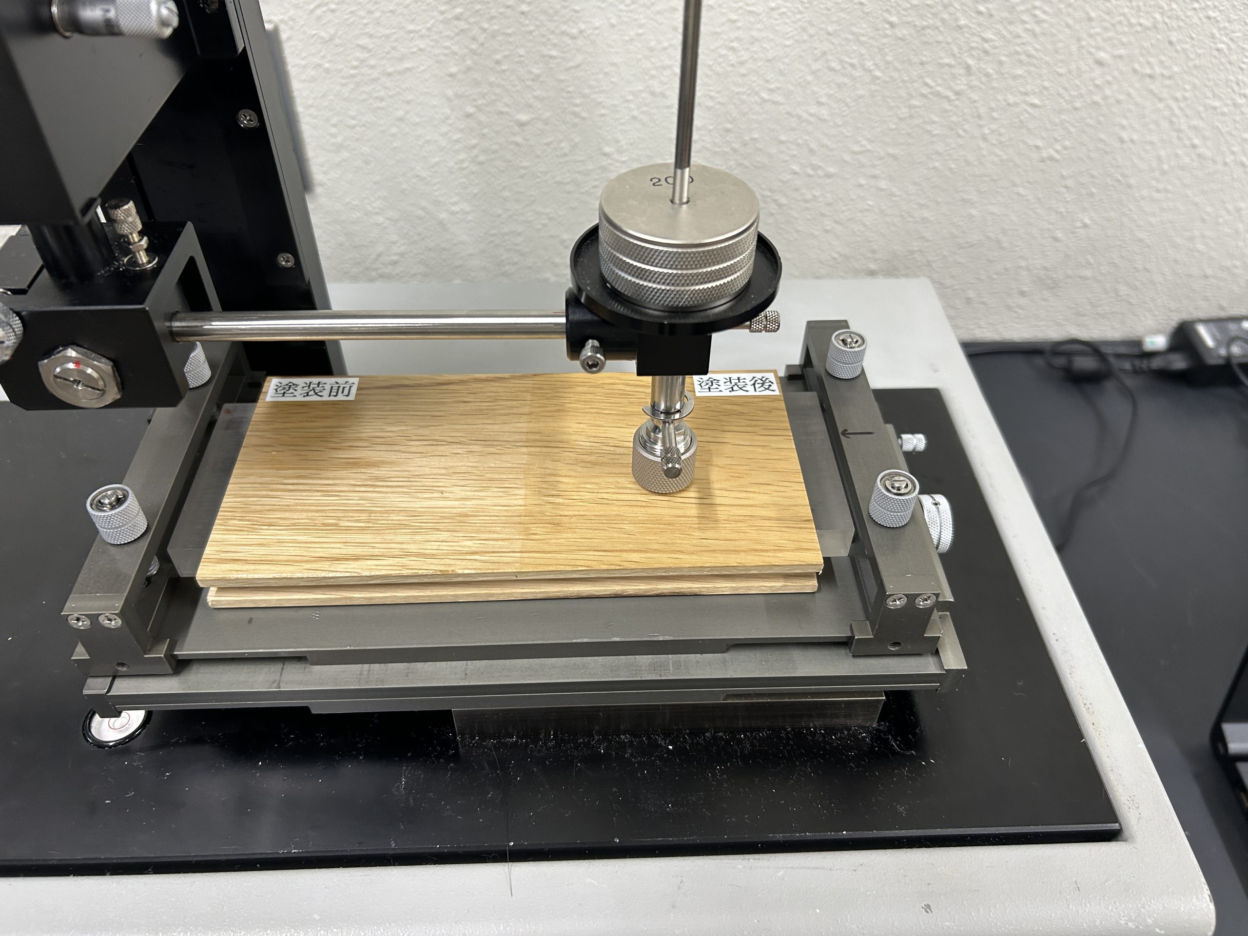 ステージに固定したナラ材サンプルを5ミリ移動させて摩擦力を測定する様子。塗装前と塗装後の面